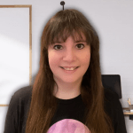 A woman with long brown hair and glasses smiles at the camera, set against a soft, light background with a hint of a modern workspace.