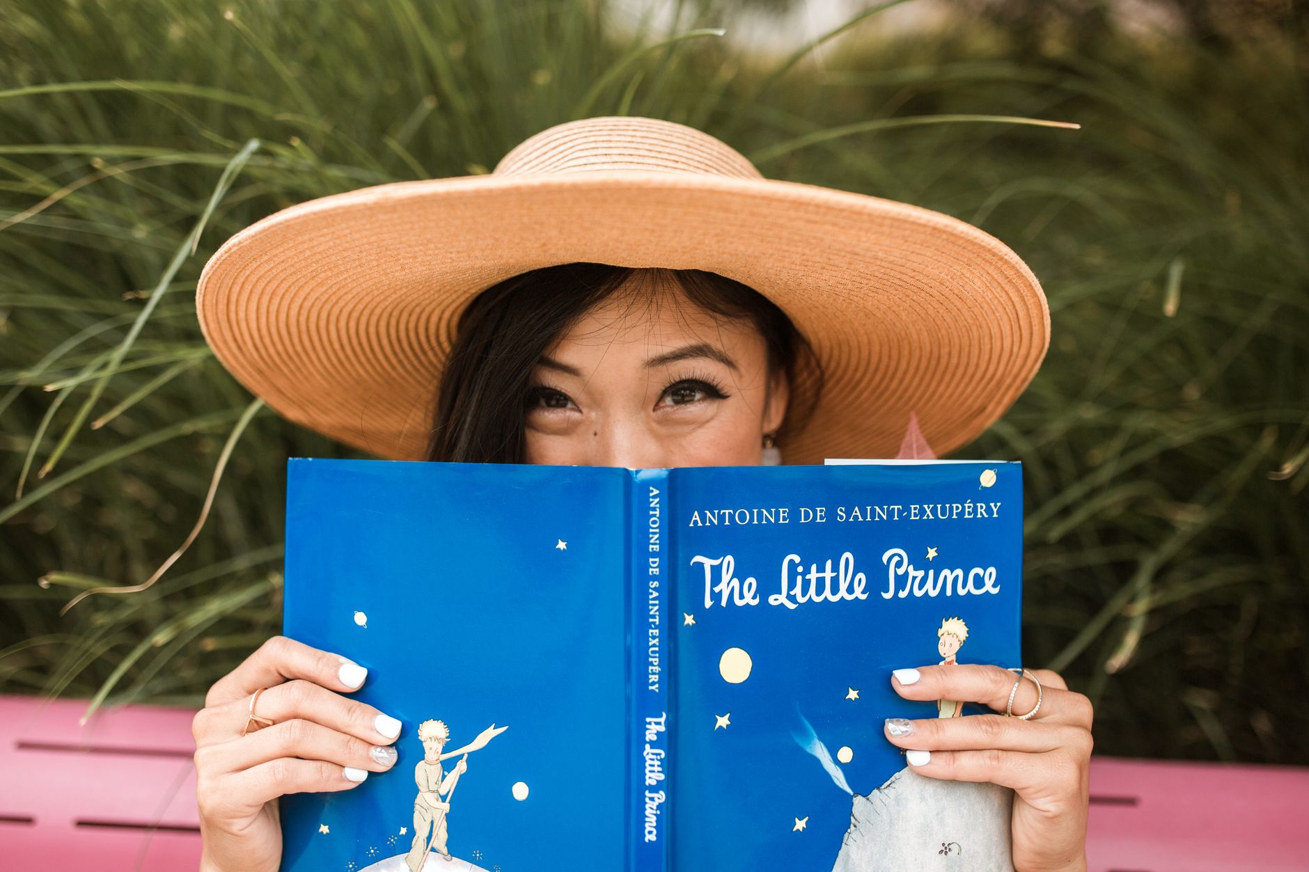 photograph of a woman with a hat covering her mouth with a blue book